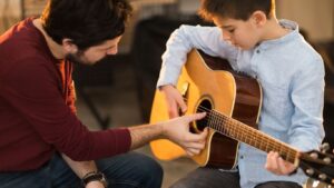 Young man teaching a boy to play the guitar.